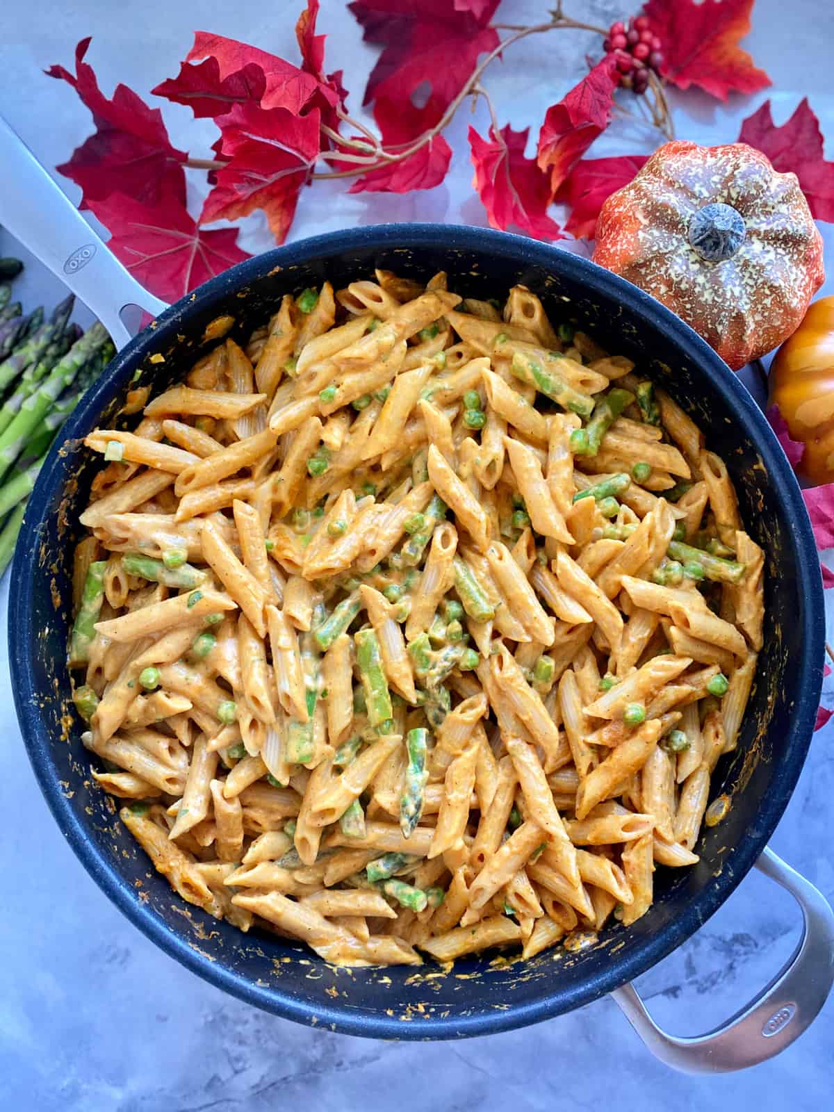Top view of a large skilelt filled with creamy orange pasta with peas and asparagus.