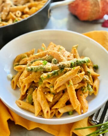 White bowl filled with pumpkin pasta, peas, and asparagus.