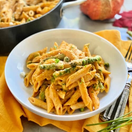 White bowl filled with pumpkin pasta, peas, and asparagus.