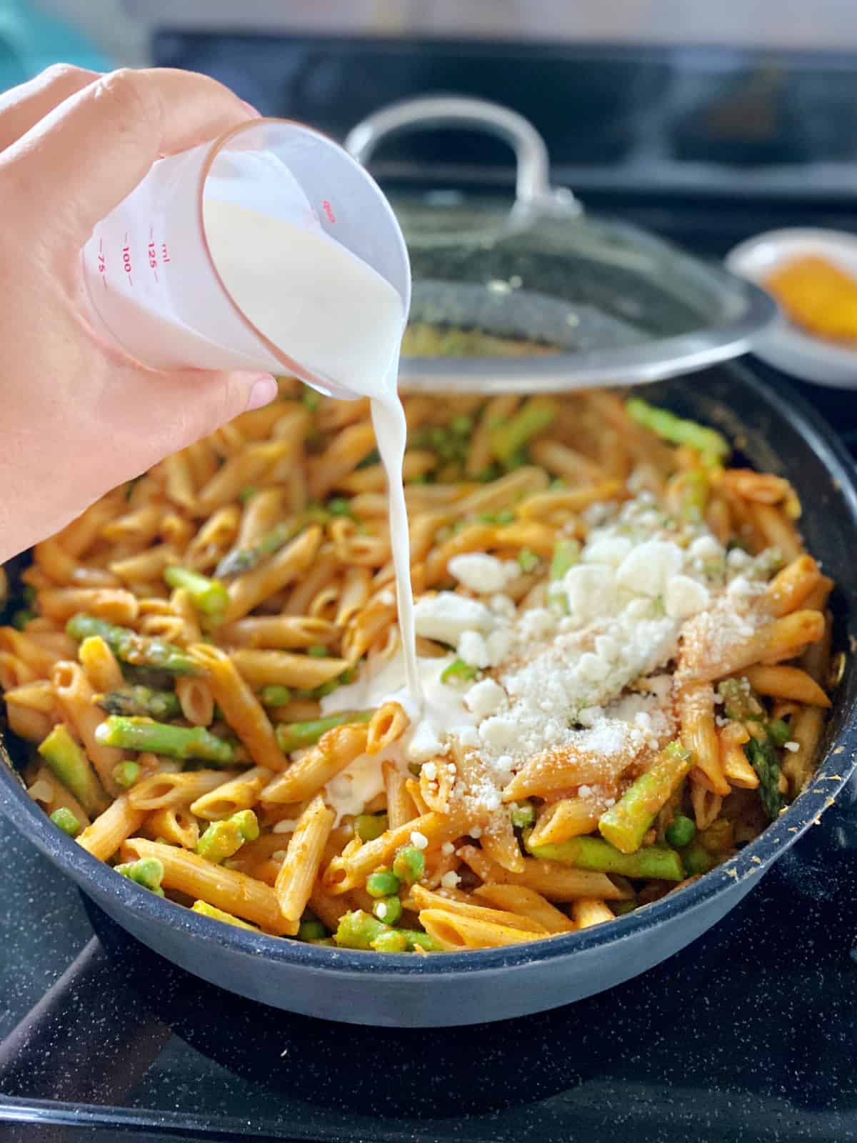 Female hand pouring heavy cream into a pasta skillet.