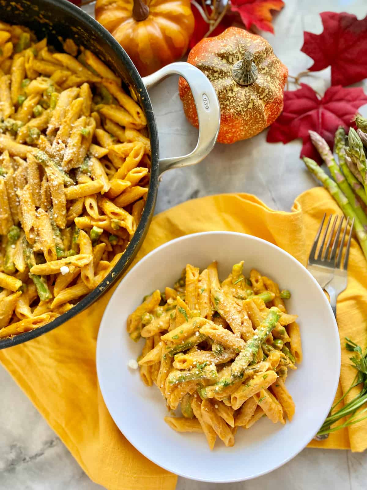 Top view of a white bowl filled with creamy penne pasta with a large skillet filled with pasta next to it.