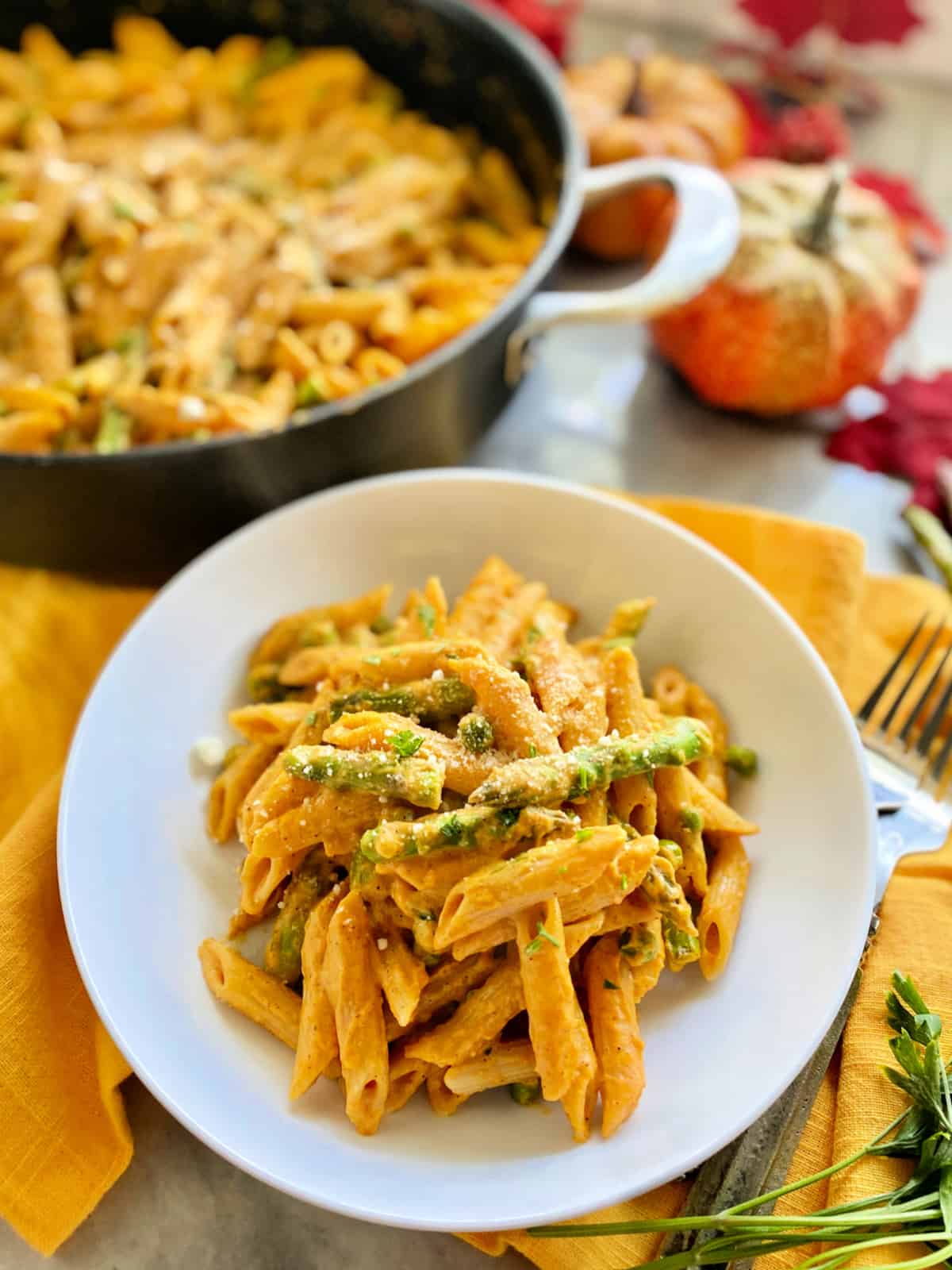 White shallow bowl filled with orange pasta with asparagus, peas, on a yellow napkin.