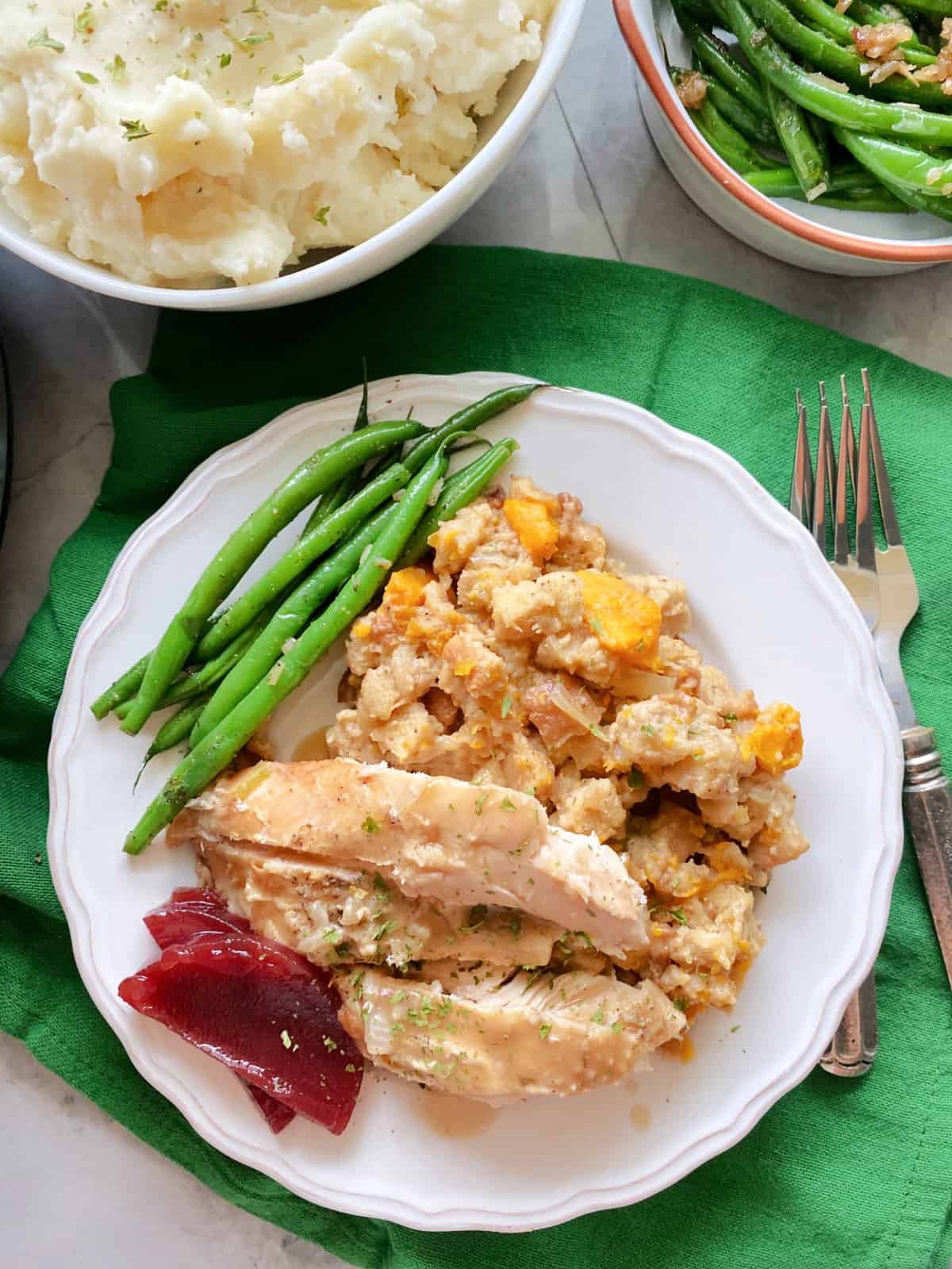 Top view of a white plate filled with turkey, stuffing, green beans, and mashed potatoes on the side.