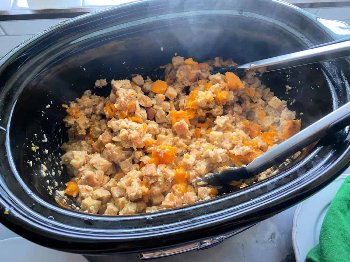 Black slow cooker filled with stuffing and tongs.