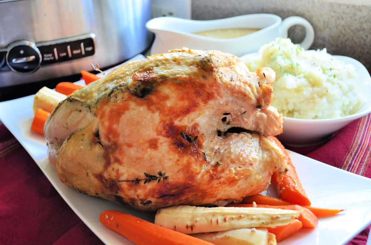 Whole turkey breast browned with parsnips and carrots on a white platter.