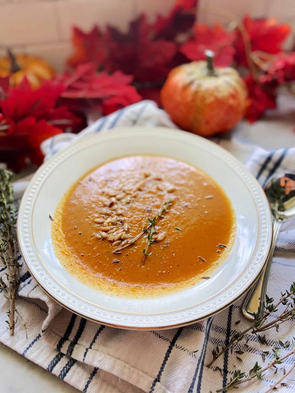 Close up of a white china plate filled with an orange squash soup with seeds and thyme sprigs.