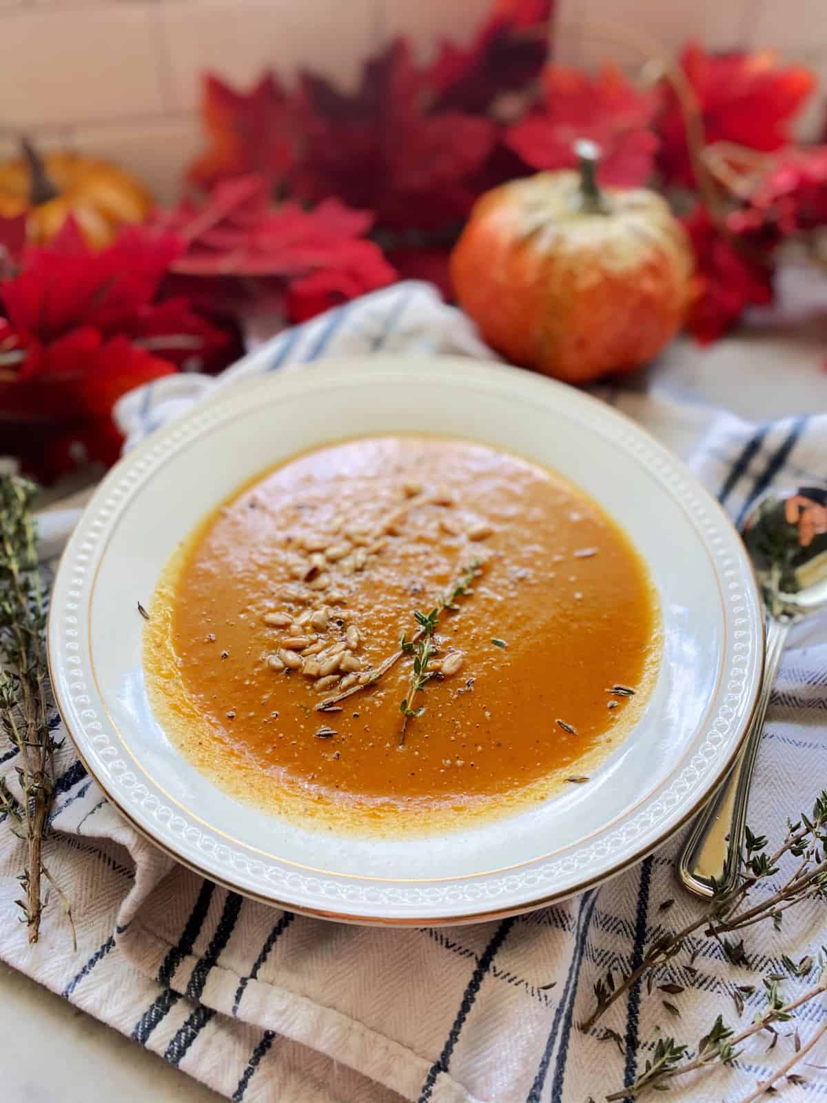 Close up of a white china plate filled with an orange squash soup with seeds and thyme sprigs.