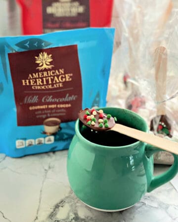 Green mug with a chocolate spoon with sprinkles resting on top with American Heritage chocolate bags in background.