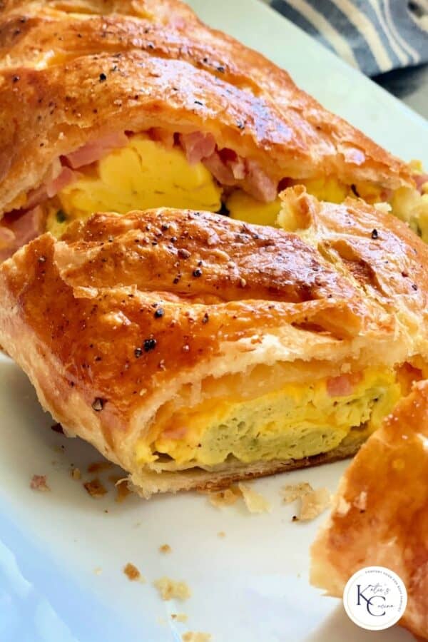 Close up of sliced puff pastry filled with egg, ham, and cheese with logo on bottom right corner.