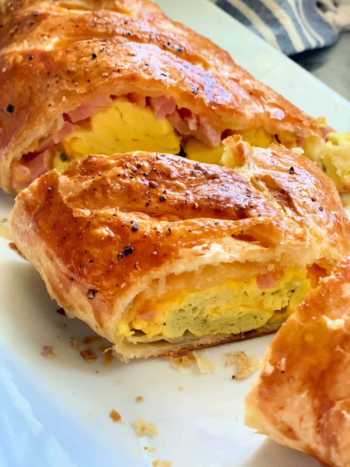 Close up of Three slices of puff pastry filled with egg, ham, and cheese on a white plate.