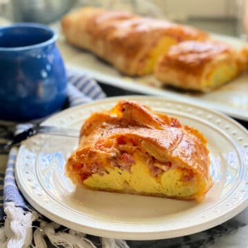 Square picture of a white plate filled with a slice of egg and ham puff pastry with a full pastry in background.