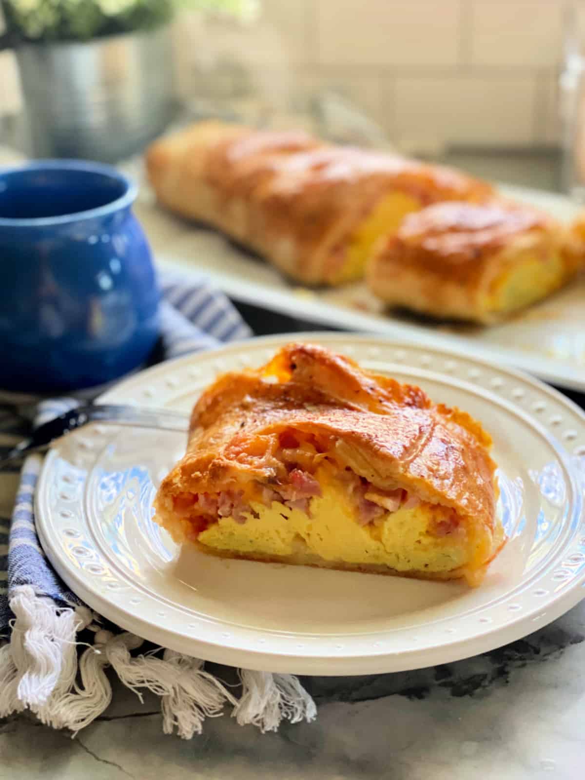 White plate with a slice of puff pastry, eggs, ham, and cheese with a fork on the plate.