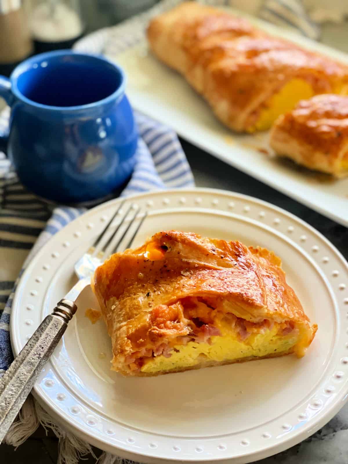 White plate filled with puff pastry, eggs and ham with puff pastry on a platter in the background.