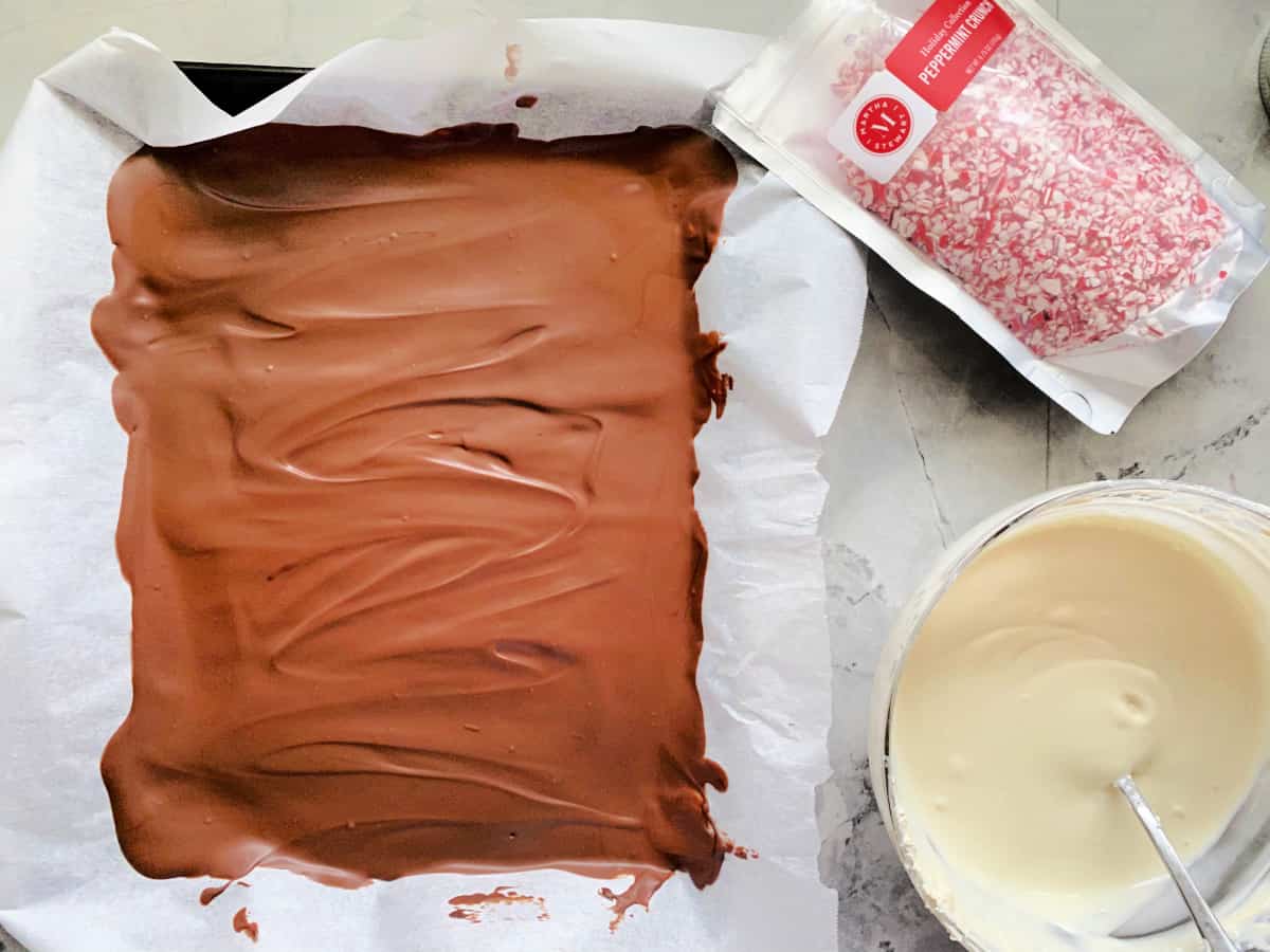 Top view of a hardened chocolate in a baking tray with melted white chocolate and chopped peppermint.