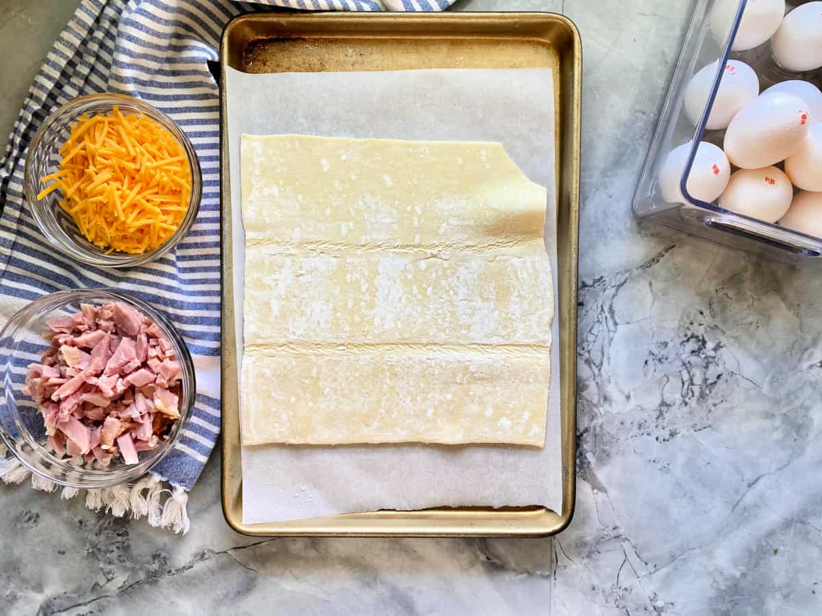 Top view of a baking baking sheet lined with parchment and a sheet of puff pastry on top.