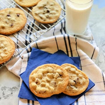 2 chocolate chip cookies on two bright blue paper napkins on top of a striped white and blue dish cloth.