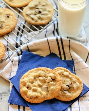 2 chocolate chip cookies on two bright blue paper napkins on top of a striped white and blue dish cloth.