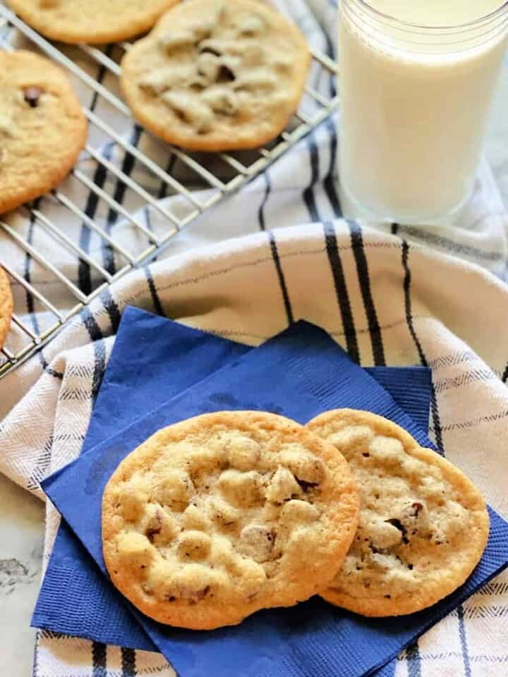 2 chocolate chip cookies on two bright blue paper napkins on top of a striped white and blue dish cloth.