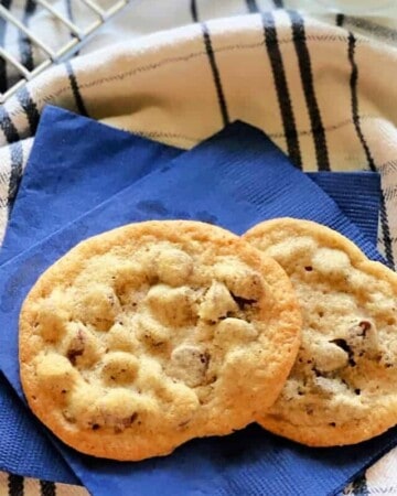 2 chocolate chip cookies on two bright blue paper napkins on top of a striped white and blue dish cloth.