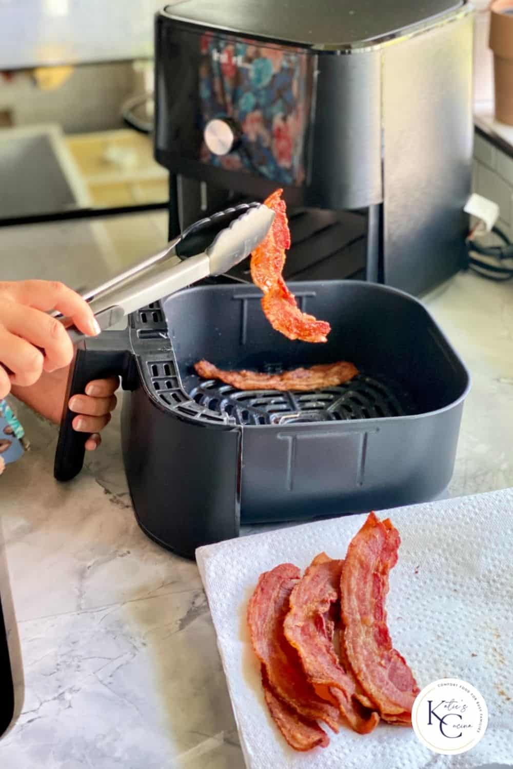 bacon in air fryer basket removed by tongs and placed on paper towel
