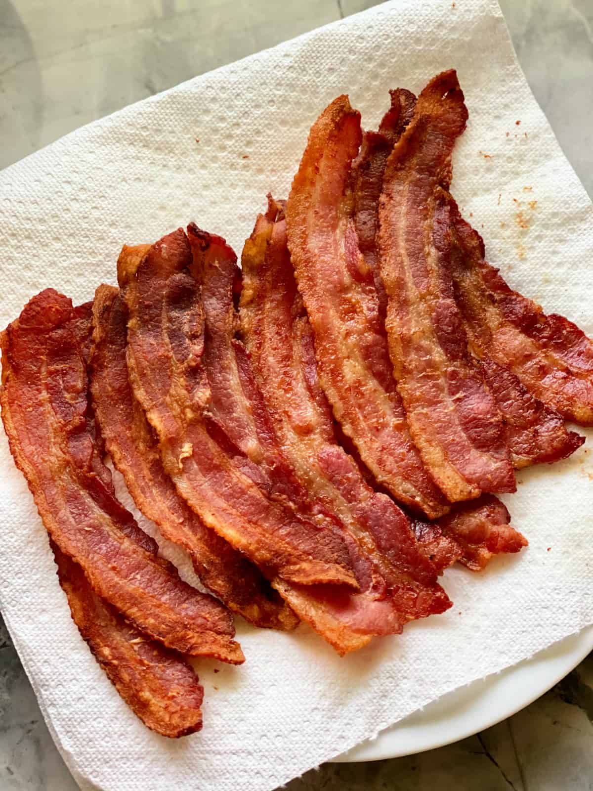 Eleven cooked slices of bacon resting on paper towel