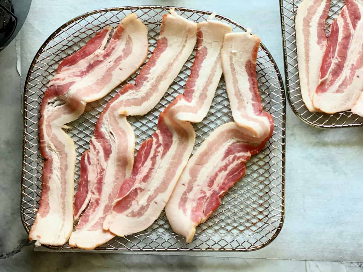 Four uncooked slices of bacon on mesh rack