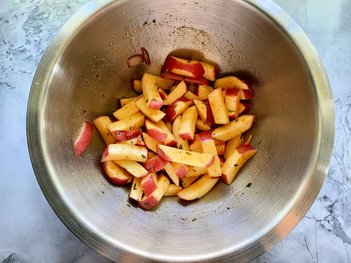 Top view of potato slices and seasoning in mixing bowl