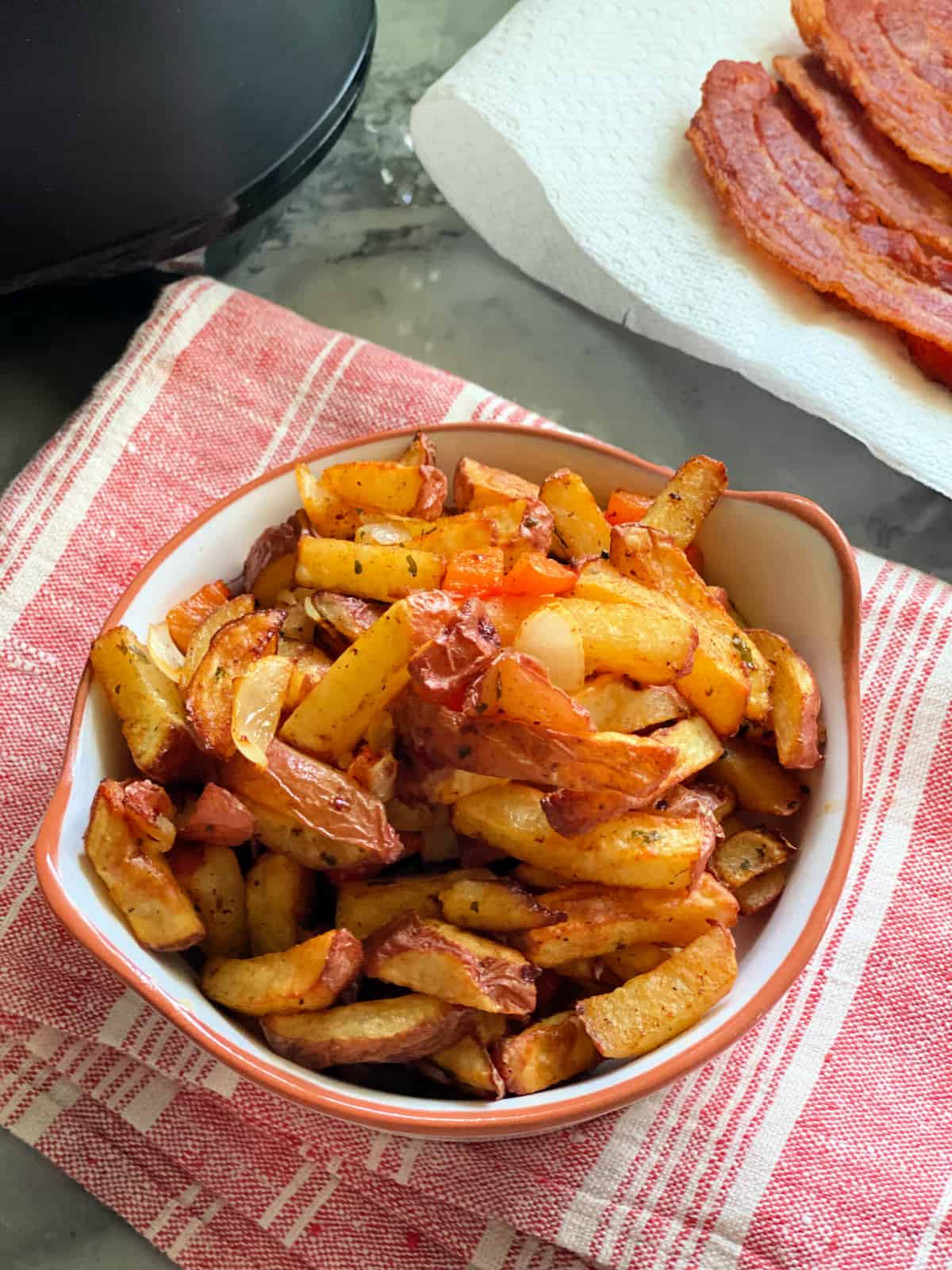 Top view of White dish with fried breakfast potatoes inside sitting on red and white towel white dish with fried breakfast potatoes inside sitting on red and white towel