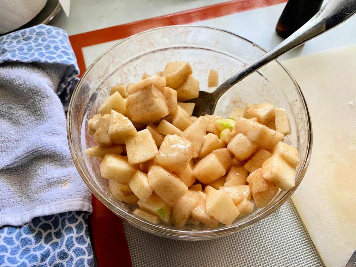 Glass bowl with chopped apple and pears mixed with cinnamon and sugar.