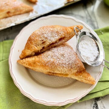 Two triangel turnovers on a white plate with a powder sugar sifter resting next to it.