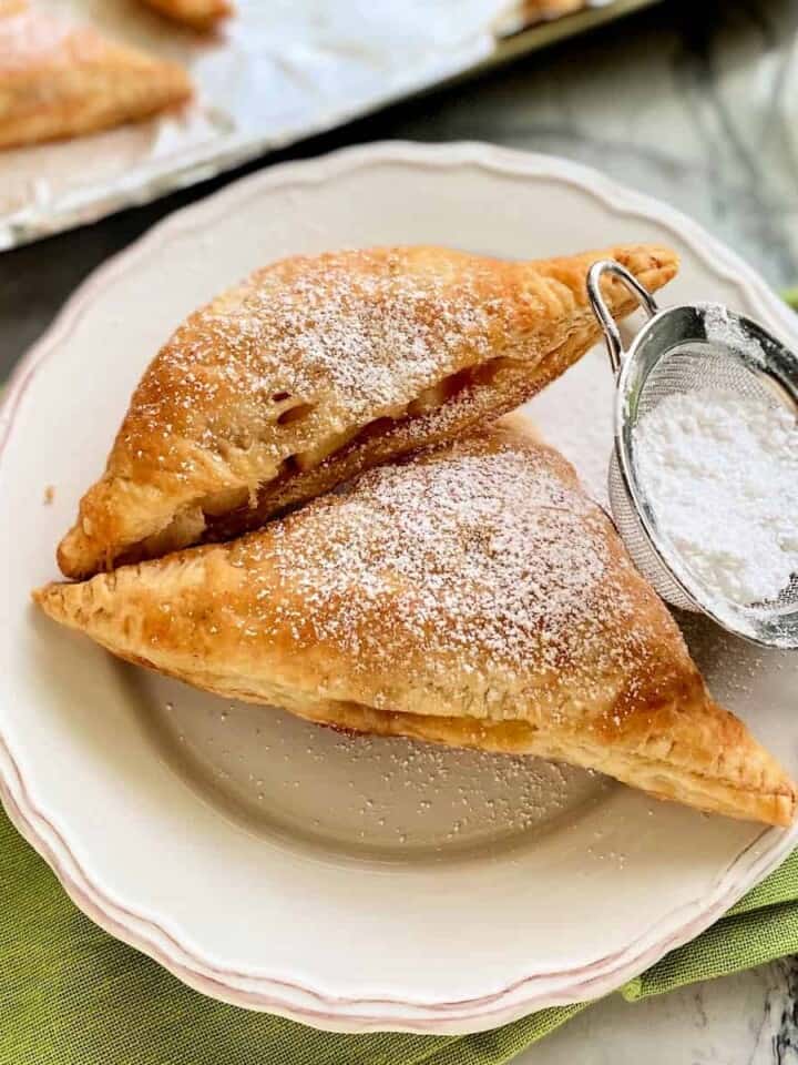 Two triangel turnovers on a white plate with a powder sugar sifter resting next to it.