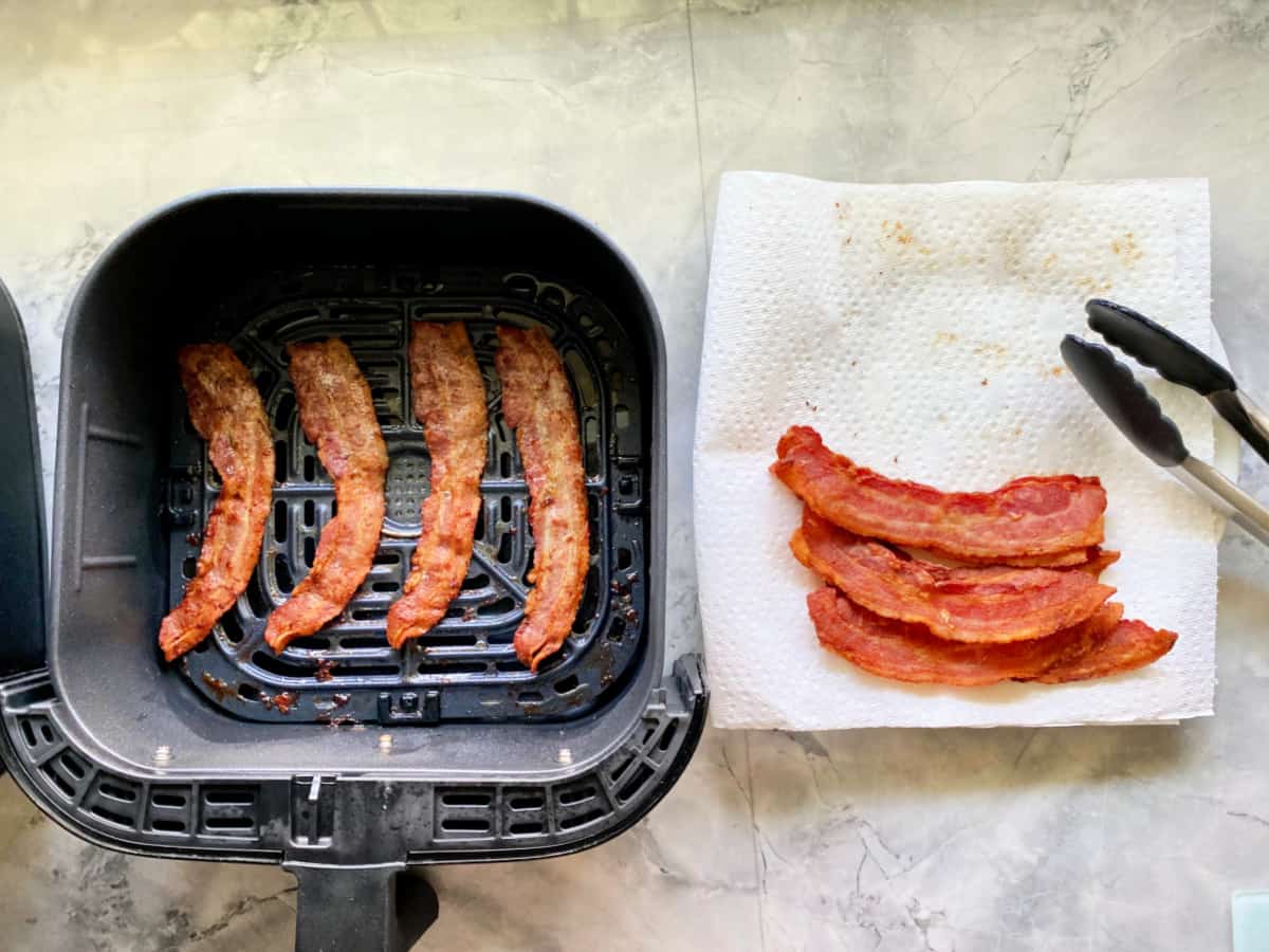 Bacon in air fryer basket with tongs on the side