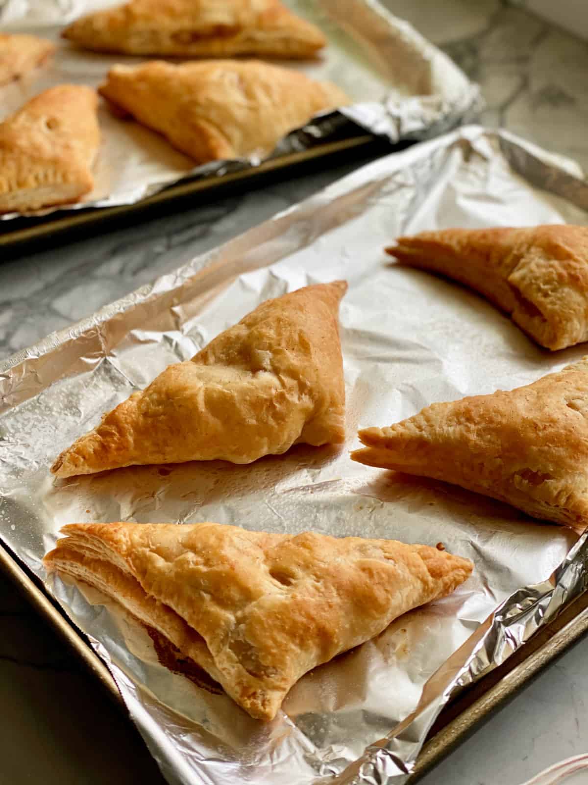 Two baking trays lined with foil with four baked turnovers on each.