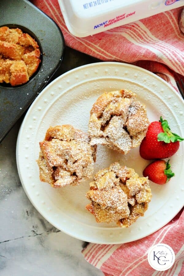 Top view of three French toast muffins on white plate with strawberries