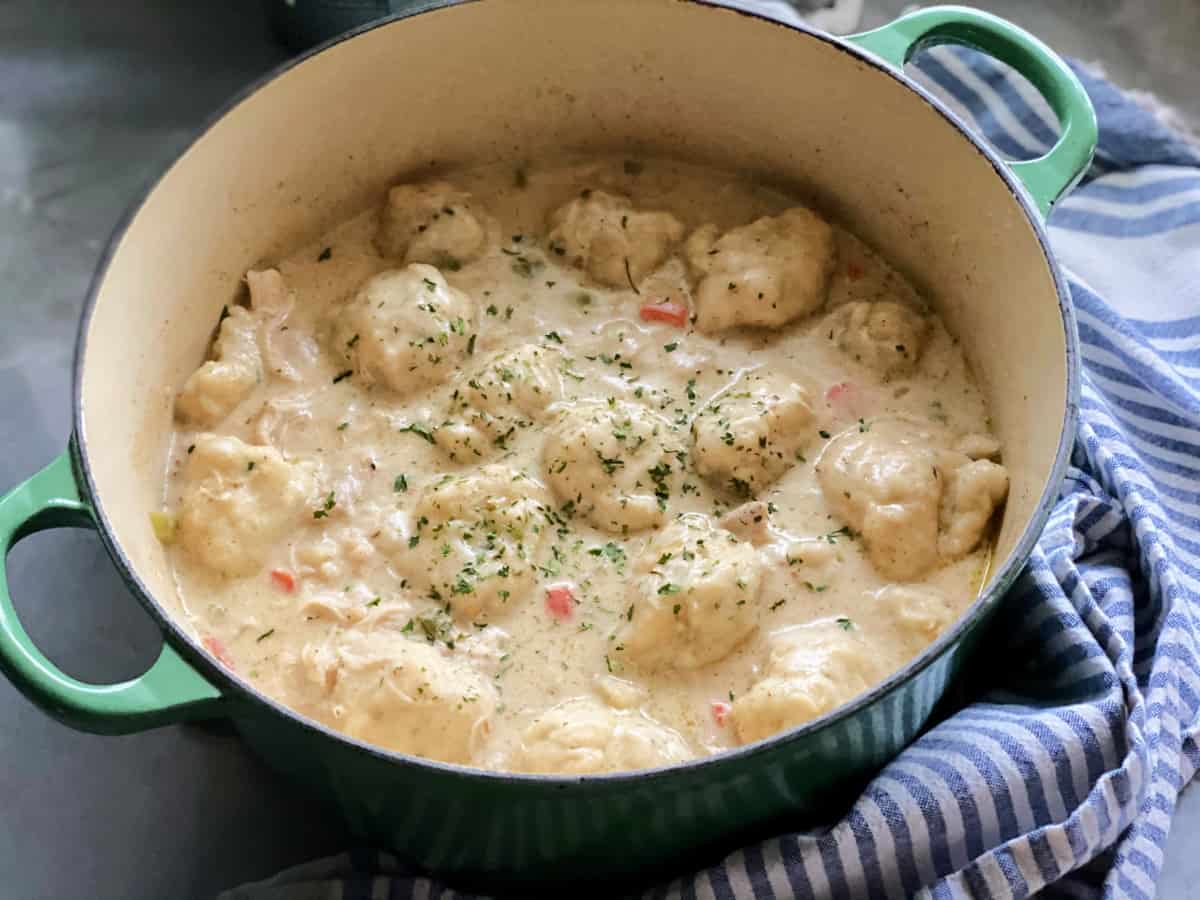 Chicken and dumpling soup in green dutch oven on top of blue and white kitchen towel