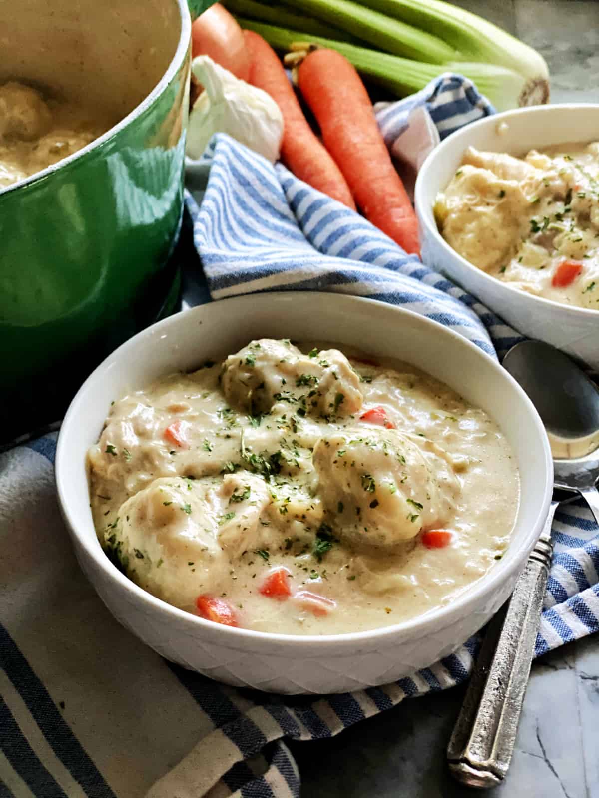 Chicken and dumpling soup in white bowl sitting on top of blue and white towel with green dutch oven in background