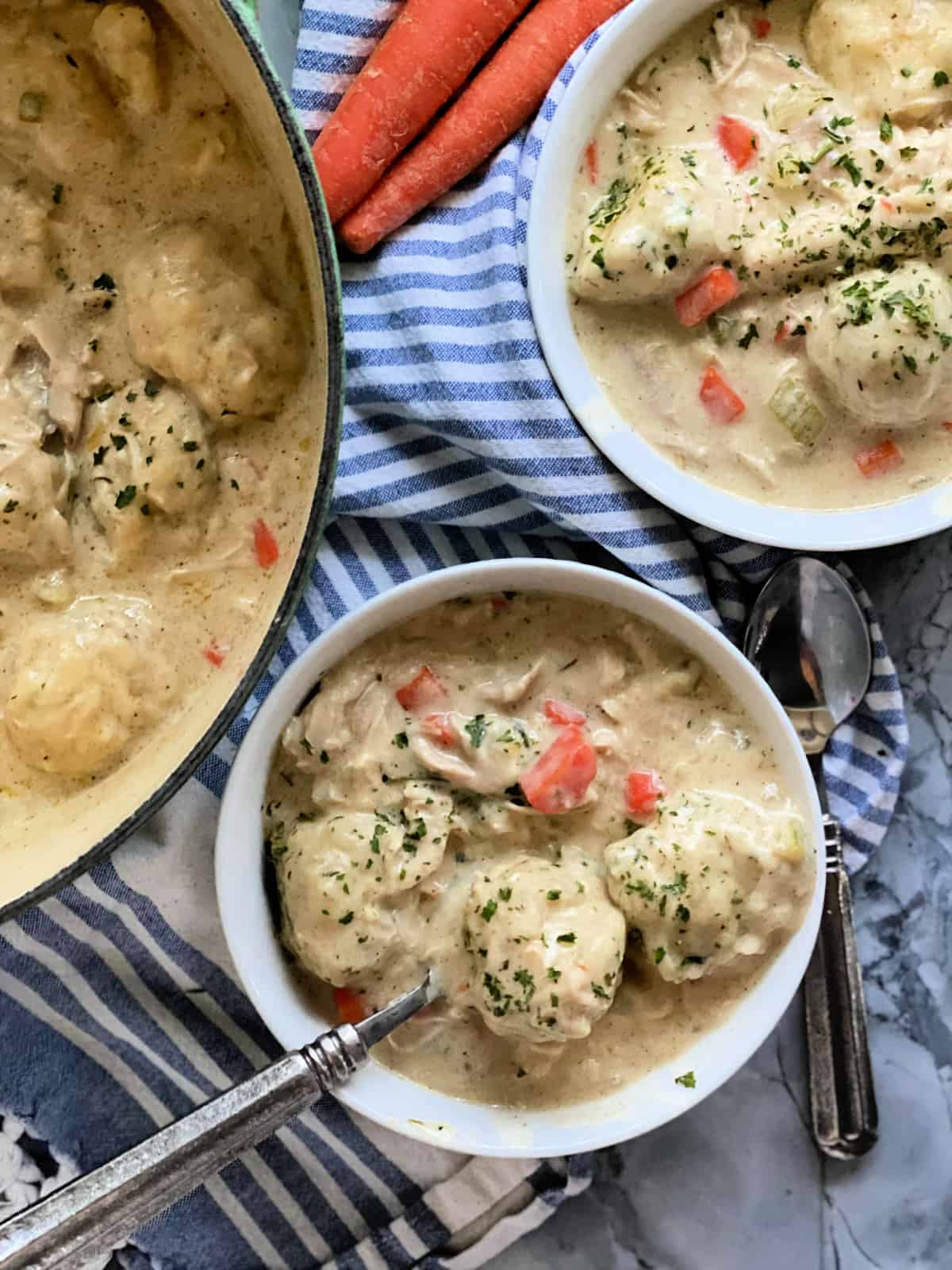 Chicken and dumpling soup in white bowl sitting on top of blue and white towel with green dutch oven in background