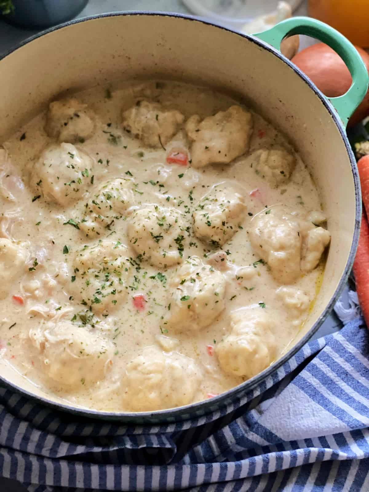 Chicken and dumpling soup in green dutch oven sitting on top of blue and white kitchen towel