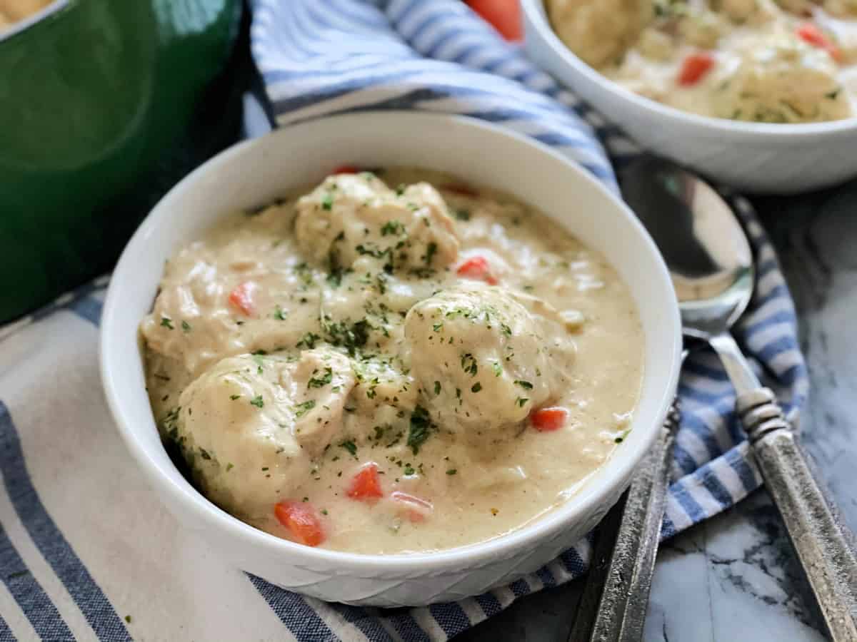 White bowl of chicken and dumpling soup on top of blue and white towel