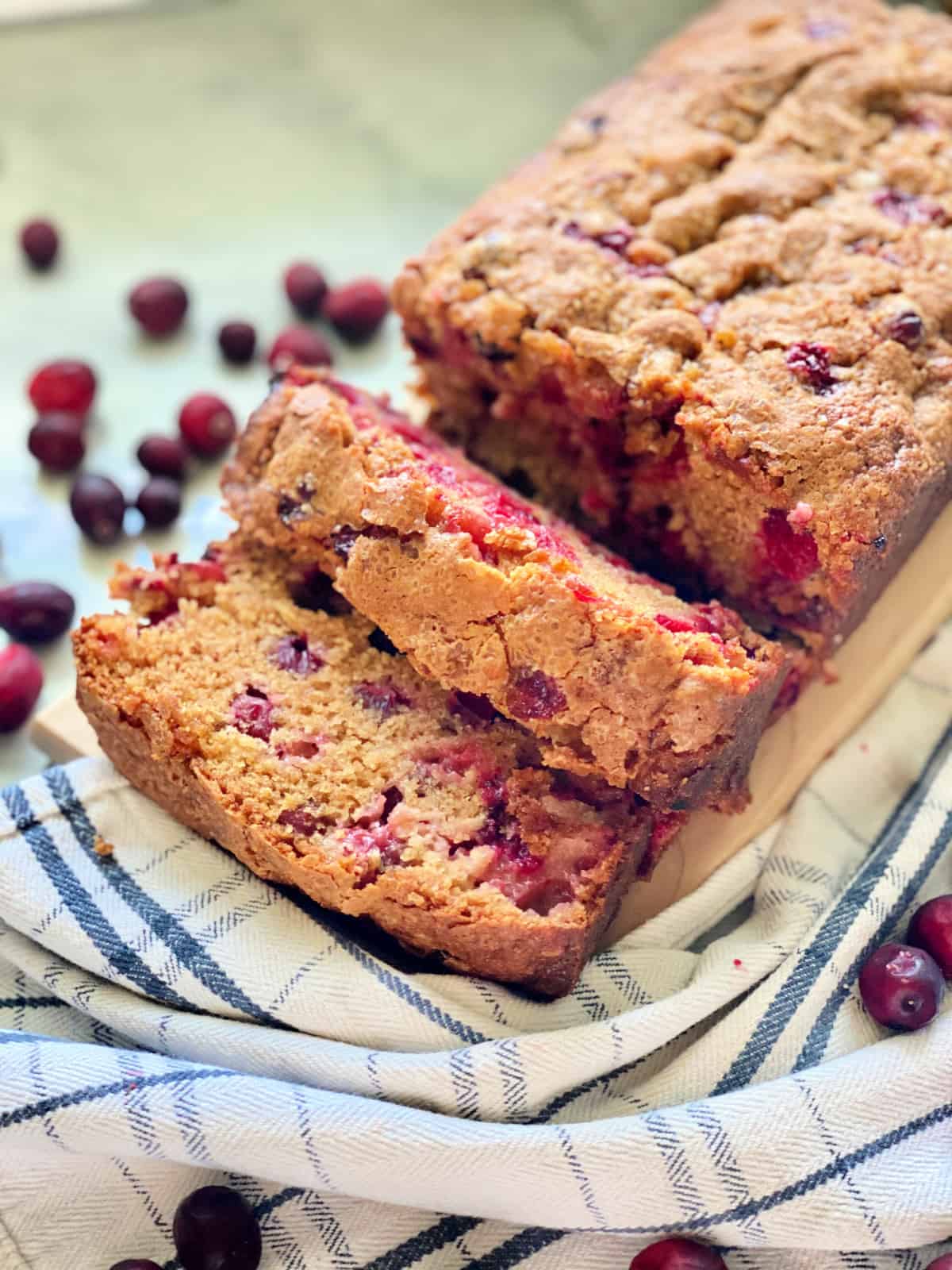 Top view of a loaf of bread with two slices and cranberries scatter on countertop.