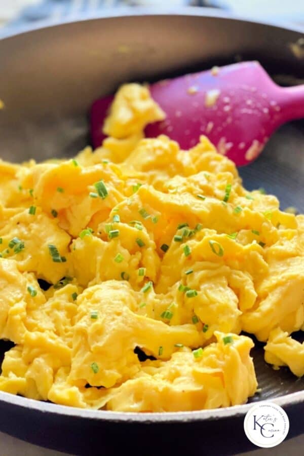 Frying pan with scrambled eggs in pan with pink spatula and logo on right bottom corner.