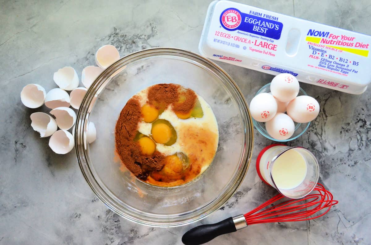 Top view of mixing bowl with eggs, cream, milk, and spices inside and eggs on the side