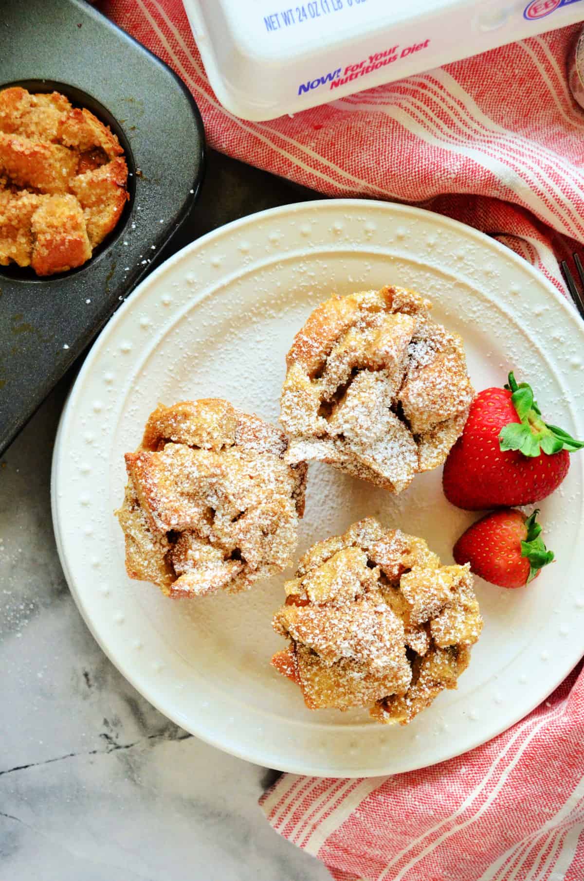 Top view of french toast muffins with powdered sugar and fruit on white plate with title text on bottom