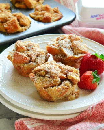 Square photo of a white plate with three french toast muffins and strawberries.