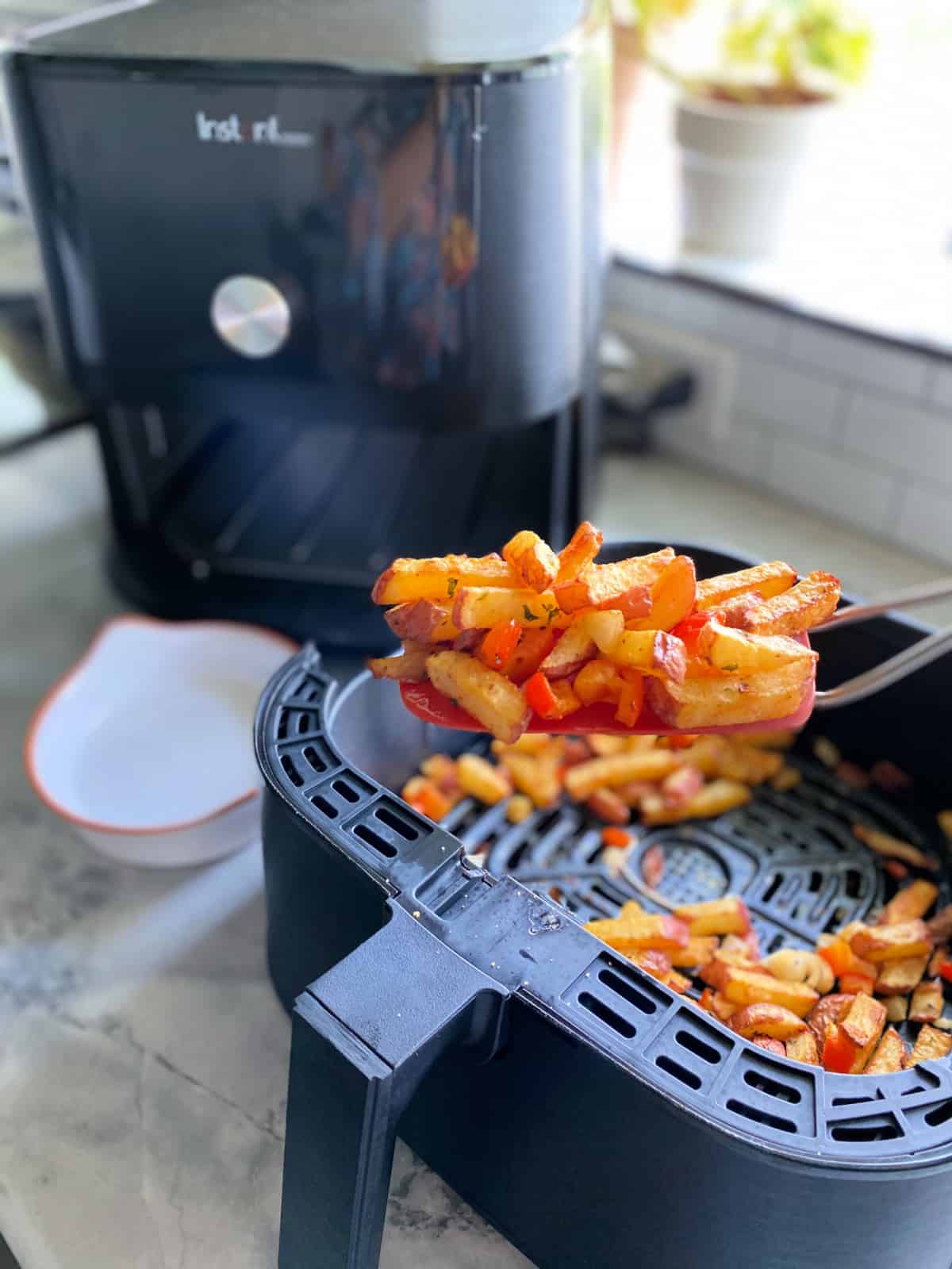Cooked potato slices being taken out of an air fryer with spatula
