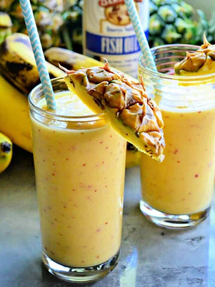 Two yellow smoothies with pineapple on the rim and paper blue straws.