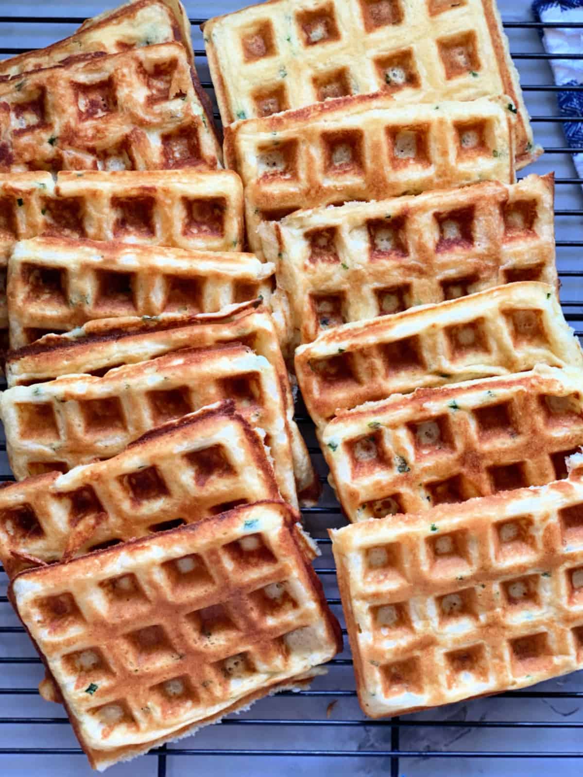Top view of 14 waffles stacked on a wire rack cooling.