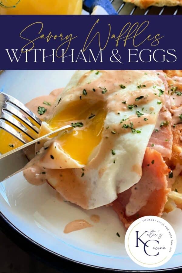 Close up shot cutting into egg stacked on ham and waffles with sauce, recipe title text at top of image