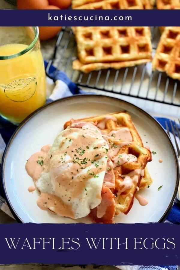 White plate with two waffles, ham, and an egg on top with a sauce drizzle