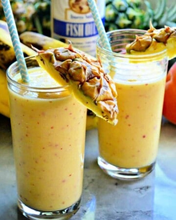 Two yellow smoothies with pineapple on the rim and paper blue straws.